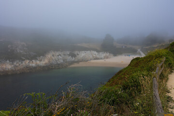 Fog stands over a sandy beach with blue water overlooking the beach from afar, a bay or bay for...