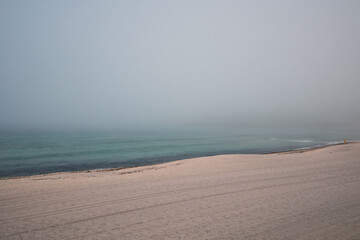 Obraz premium Sandy beach in heavy fog without people. The ocean is turquoise in color.