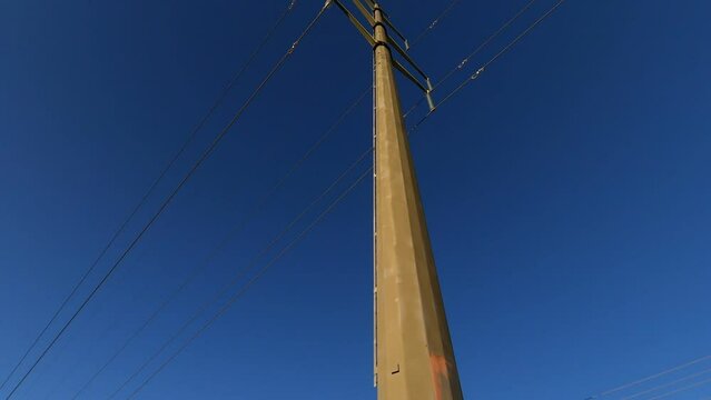 Single electrical tower and power lines against dark blue sky, tilt up, rotate; in Ontario, Canada.