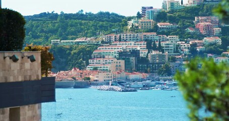 Resort city on hills at bright sunlight creating mild fog and surrounded by sea water. Ships and boats moored at beach attract tourist attention