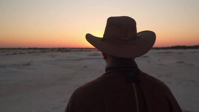 close up of a man dressed as a cowboy standing on a salt field watching the sunrise
