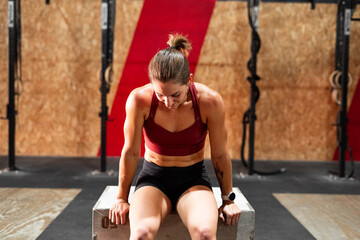 Fototapeta na wymiar sporty muscular brunette caucasian girl doing sports sitting on a big wooden box in a gym