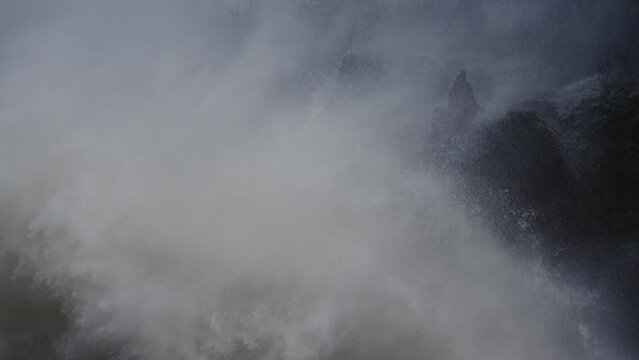 Rough ocean wave crash against rocky cliff on a gloomy stormy day, slow motion