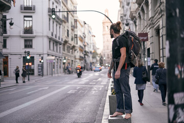 caucasian guy with beard long hair t-shirt and blue pants barefoot in the street of a city, valencia, spain