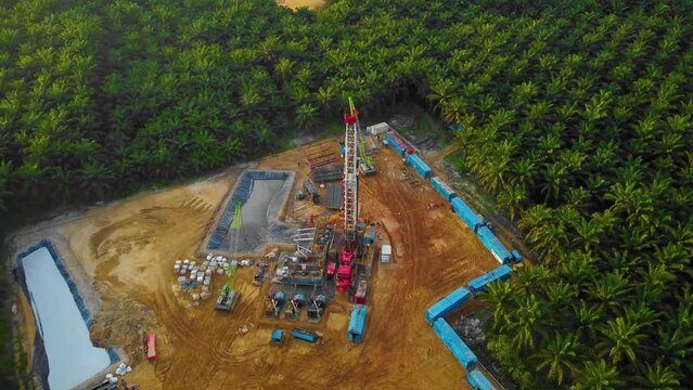 Cinematic 4K Drone Footage of Onshore Drilling Rig equipment structure for oil exploration and exploitation in the middle of jungle surrounded by palm oil trees during sunset and high oil price.