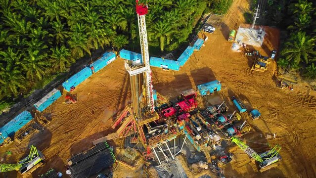 Cinematic 4K Drone Footage of Onshore Drilling Rig equipment structure for oil exploration and exploitation in the middle of jungle surrounded by palm oil trees during sunset and high oil price.