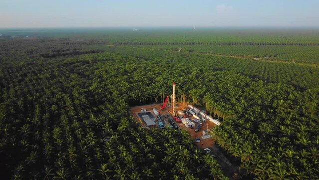 Cinematic 4K Drone Footage of Onshore Drilling Rig equipment structure for oil exploration and exploitation in the middle of jungle surrounded by palm oil trees during sunset and high oil price.
