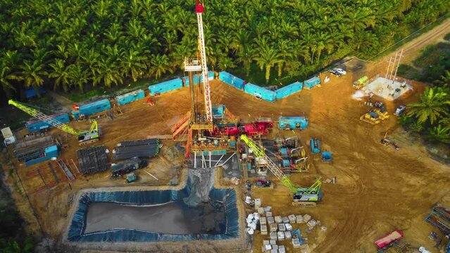Cinematic 4K Drone Footage of Onshore Drilling Rig equipment structure for oil exploration and exploitation in the middle of jungle surrounded by palm oil trees during sunset and high oil price.