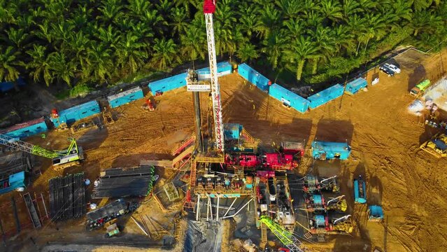 Cinematic 4K Drone Footage of Onshore Drilling Rig equipment structure for oil exploration and exploitation in the middle of jungle surrounded by palm oil trees during sunset and high oil price.