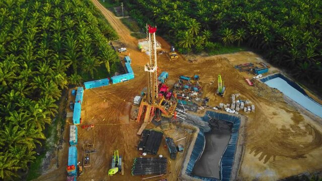 Cinematic 4K Drone Footage of Onshore Drilling Rig equipment structure for oil exploration and exploitation in the middle of jungle surrounded by palm oil trees during sunset and high oil price.