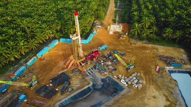 Cinematic 4K Drone Footage of Onshore Drilling Rig equipment structure for oil exploration and exploitation in the middle of jungle surrounded by palm oil trees during sunset and high oil price.