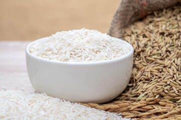 White rice grains in white bowls, white rice grains in wooden table, raw rice grains in hemp sacks and nature gold background, agricultural organic product