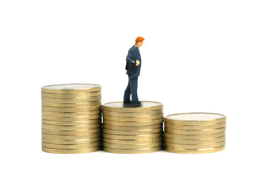 Miniature People Toy Figure Photography. Businessman Walking Above Descending Stair From Coin Pile. Isolated On White Background