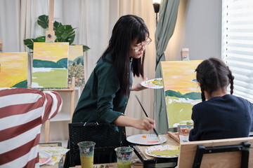 A female Asian teacher teaches and demonstrates to the children on acrylic color picture painting...