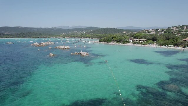 Approaching boats at Santa Giulia Beach in Corsica Island Mediterranean Sea with snorkeling tours on the rocky shores, Aerial low flyover shot