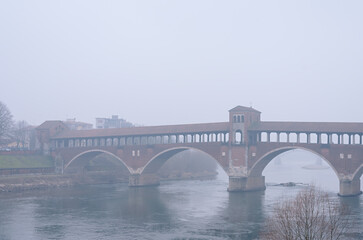 Ancient covered bridge surrounded by fog in winter. Pavia. Italy