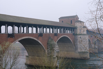 Naklejka premium Ancient covered bridge surrounded by fog in winter. Pavia. Italy