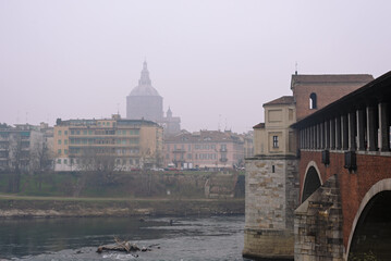 View of the Ancient Covered Bridge and the city surrounded by fog in winter. Pavia. Italy