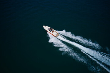 High-performance white-orange boat with people moving fast on dark blue water leave a white trail, top and top