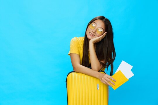 Asian woman traveling with yellow suitcase and tickets with passport in hand, tourist traveling by plane and train with luggage on blue background