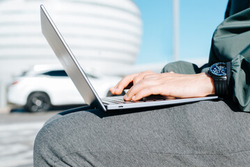 Close-up of caucasian male hands typing on laptop keyboard outdoors. Selective focus on hand with watch