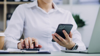 Young business woman sitting in office at table and using smartphone. On desk is laptop and tablet computer, on screen charts and graphs. Woman analyzing data. Student learning online.