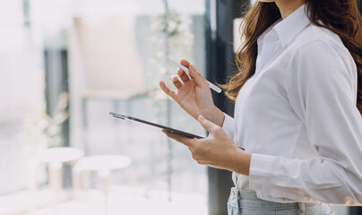Young business woman sitting in office at table and using smartphone. On desk is laptop and tablet computer, on screen charts and graphs. Woman analyzing data. Student learning online.