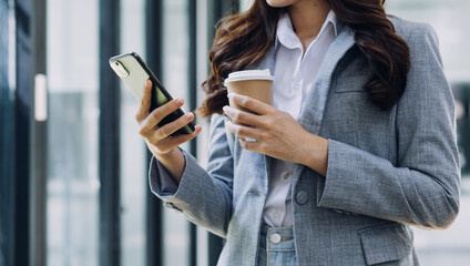 Young business woman sitting in office at table and using smartphone. On desk is laptop and tablet computer, on screen charts and graphs. Woman analyzing data. Student learning online.
