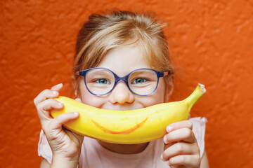 Happy little child girl with yellow banana like smile on orange background. Preschool girl with...