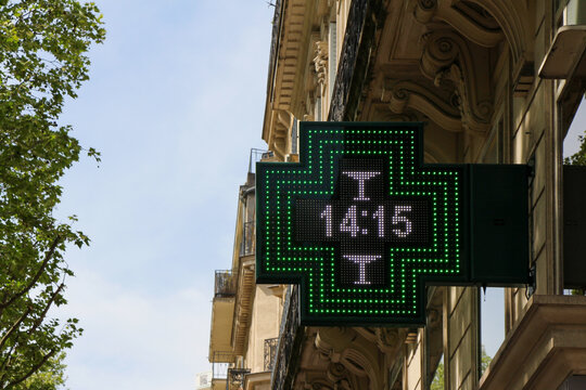 French pharmacy sign (drugstore symbol) : green cross on a parisian facade giving time (clock integrated), Paris, France.