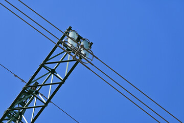 The top of the transmission tower for electrical transmission line. Close-up with glass disk insulators and electric cables. 