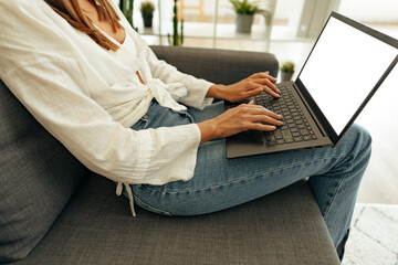 Naklejka premium Woman using laptop computer while sitting on a sofa at home.