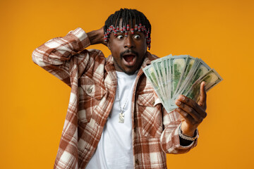 Young happy rich african man in casual shirt holding dollar bills against yellow background
