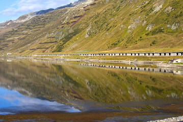 Railway station Oberalppass with lake and reflections of mountain panorama on a sunny late summer...