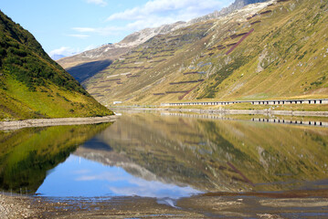 Railway station Oberalppass with lake and reflections of mountain panorama on a sunny late summer...