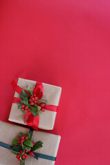 Two Christmas gifts with Holly decoration with red berries on a red background with copy space