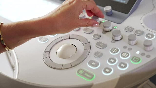 Female medic’s hand turning the handles on the medical equipment. Close up. Ultrasound machine keyboard from top view.