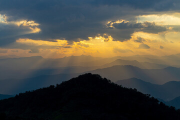  Sunset with clouds in the mountains. The sun's rays pass through the clouds late evening. Ray of the sunset with mountains and sky background. Beautiful sun beam pass through the cloud.
