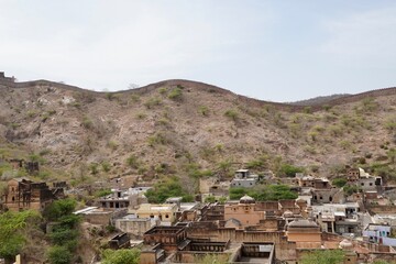 Fototapeta na wymiar Village in the mountains. Houses laid on high mountain on summer afternoon at Jaipur, India. Scenic view of mountain houses against sky.