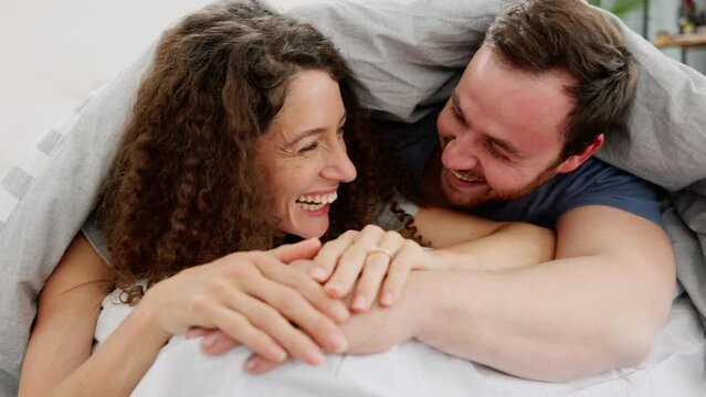 Happy, laugh and couple in bed in the bedroom of their home while laughing, bonding and holding hands. Happiness, comic joke and young man and woman relaxing together with love, care and fun at house