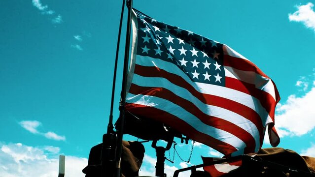 Patriotic American flag dances in the wind remidning the world that the stars and stripes represents absolute freedom and the veterans protect it as evidenced but he machine gun in the background