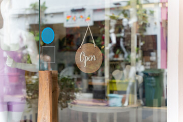 A business sign that says ‘Open’ on local businesses hang on door at entrance. Say Welcome. Open and closed flip sign in front of shop glass door.