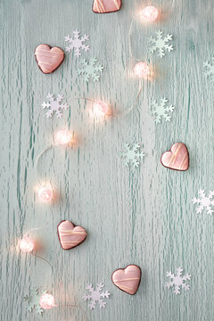 Winter pastel mint green background with paper snowflakes and string of shiny balls, electric Xmas garland and heart shape cookies. Simple minimal Winter holidays, Christmas background.