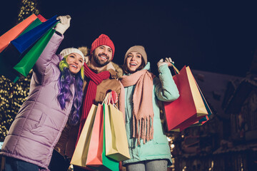 Photo of three excited positive people hold shopping packages have good mood tree garland outside