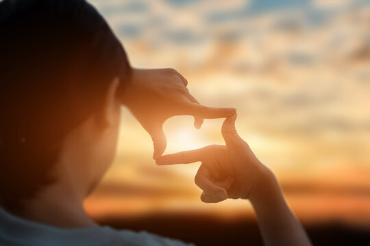 Future planning concept. Close up of young woman hands making a frame sign over sunset sky. New year planning and vision concept.