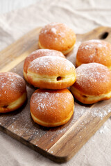 Homemade Apricot Polish Paczki Donut with Powdered Sugar on a Wooden Board, side view. Close-up.