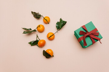 tangerines with green leaves, lying on a beige pastel background next to a green gift box. Preparation for the new year, copy space, top view. Flatlay
