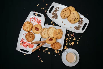 Fotobehang Top view of cookies on white plates with a cup of coffee on a black background © Diego Ignacio Riquelme Alvarado/Wirestock Creators
