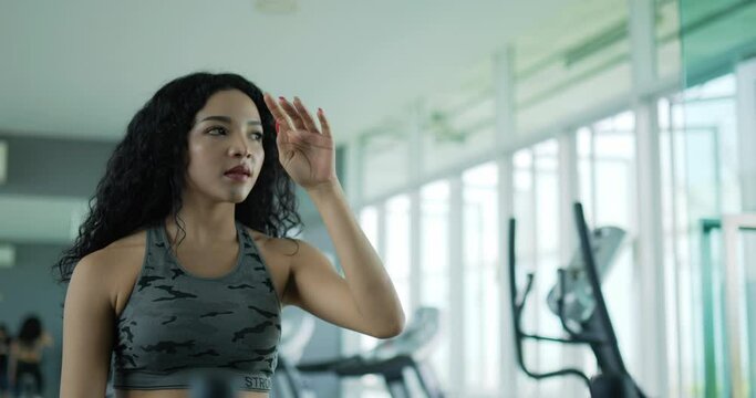 Handheld slow motion shot, Asian young woman wiping sweat during exercise for workout, break to cool down for stretch muscle or tired