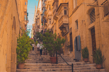Fototapeta na wymiar Picturesque streets and alleys of Valletta, Malta on summer sun. Visible long stairs and people walking on them.